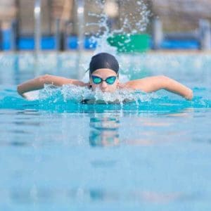 Young girl in goggles and cap swimming butterfly stroke