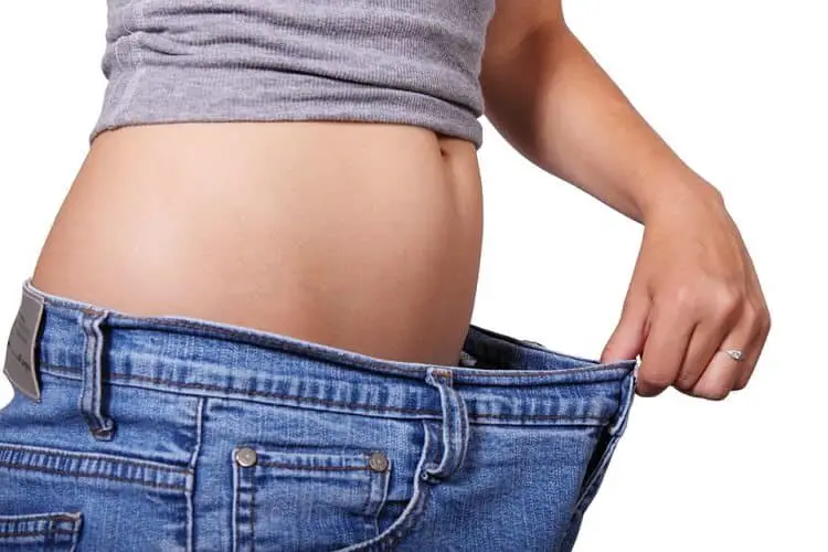 woman in grey top and jeans showing her weight loss